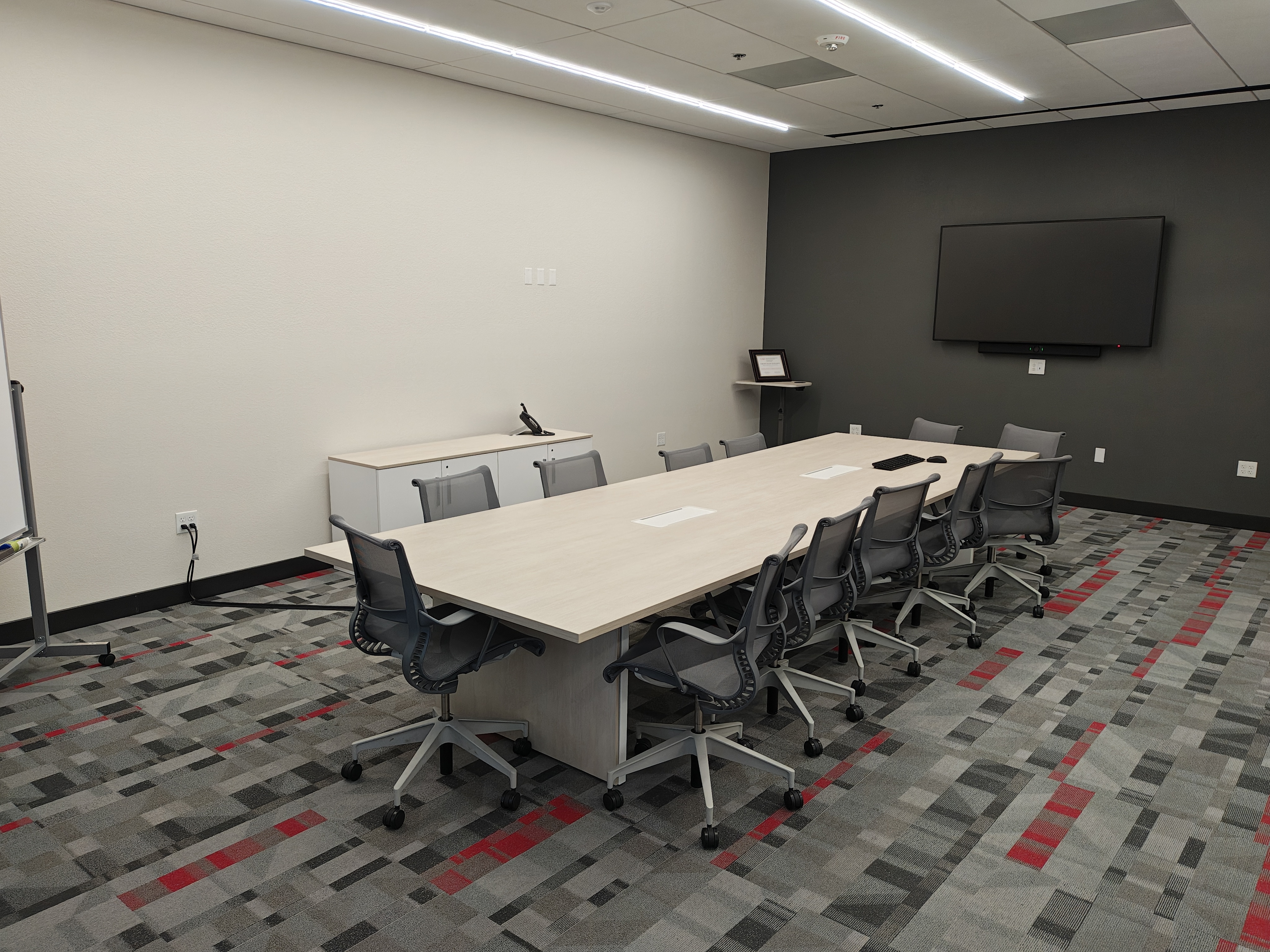 An empty conference room with a central table, chairs, and a TV screen