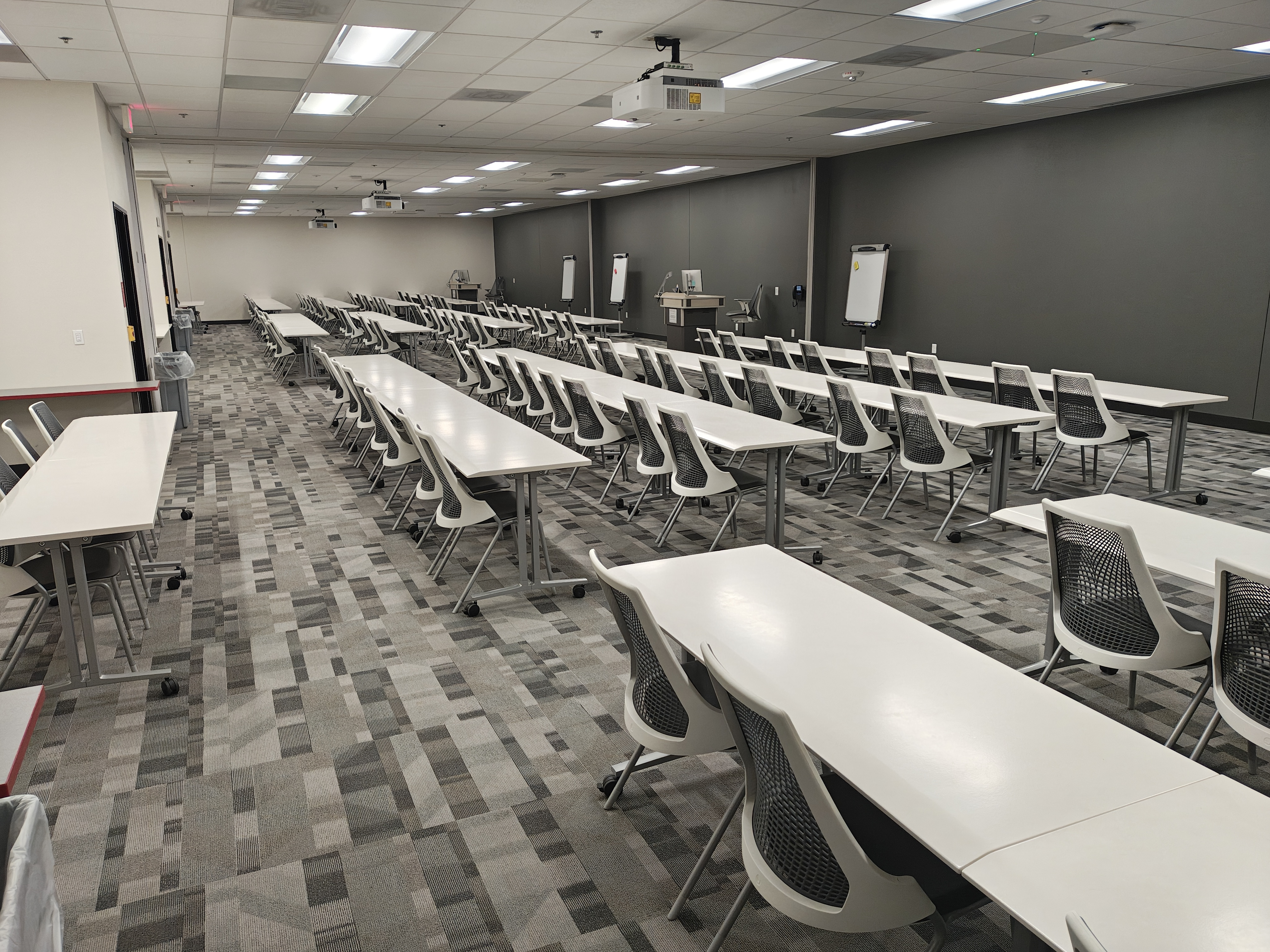 A large empty classroom with rows of tables and chairs and two lecterns 