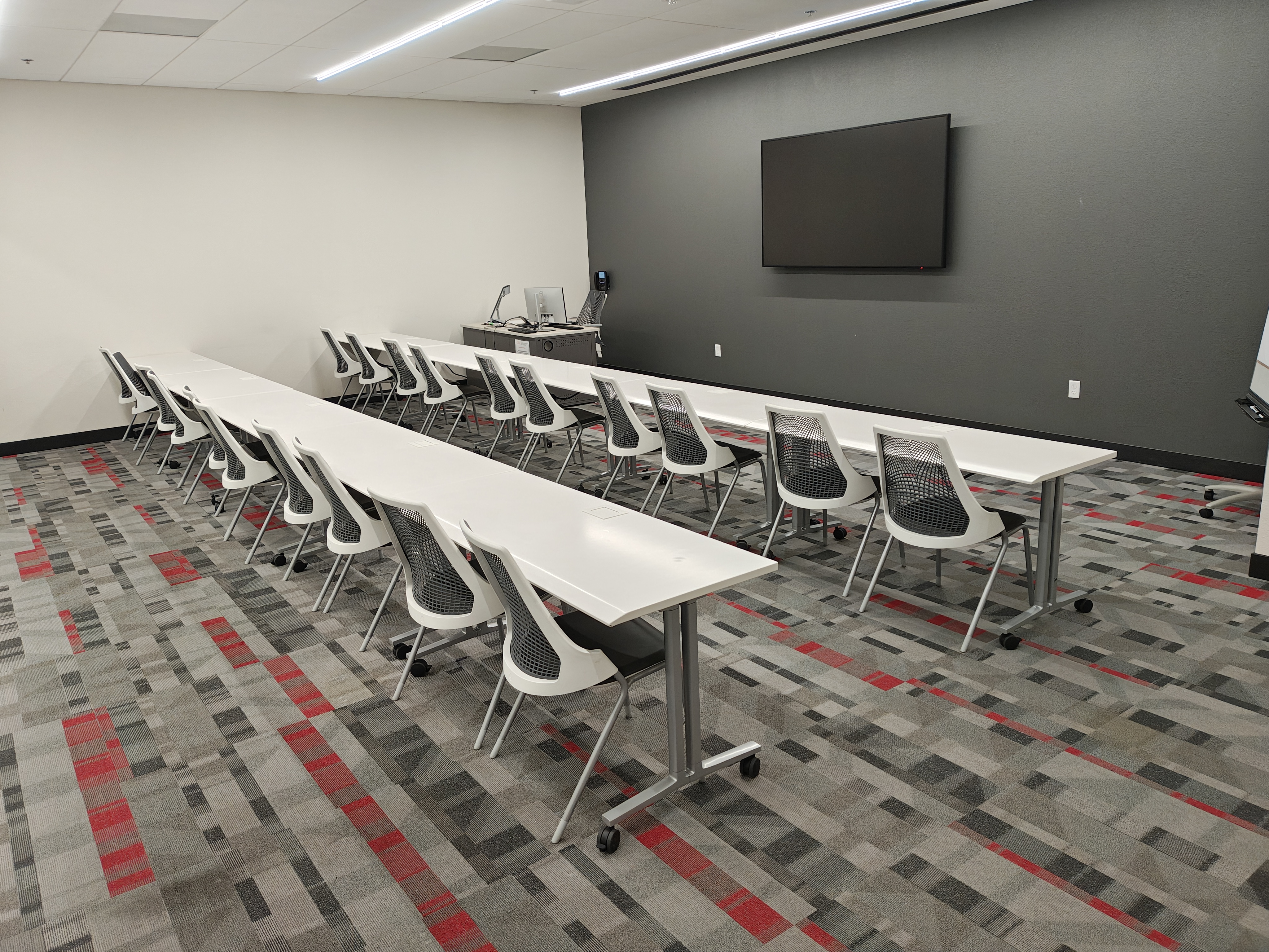 Empty classroom with rows of chairs and tables and a TV screen 