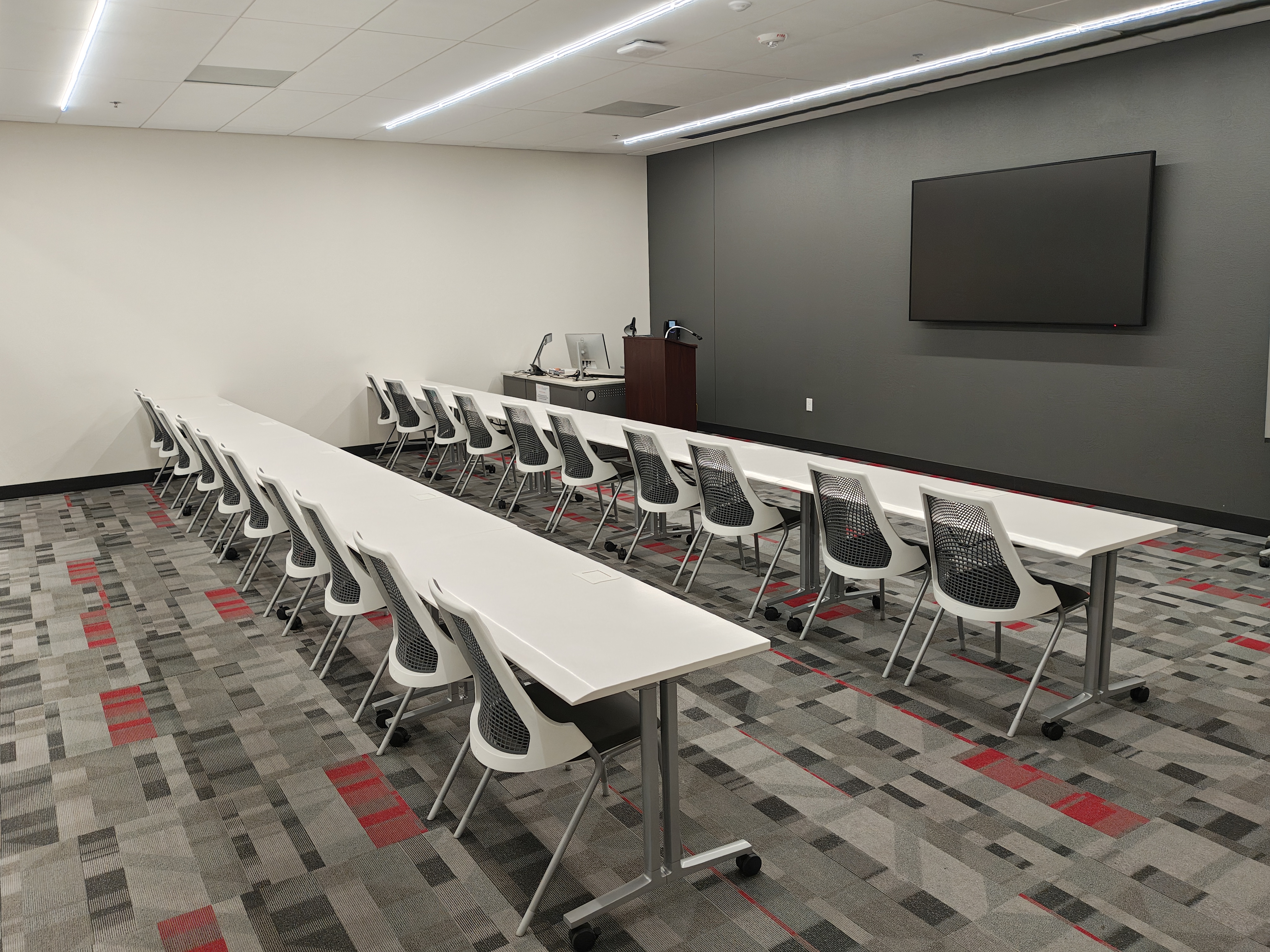 Empty classroom with rows of chairs and tables and a TV screen 