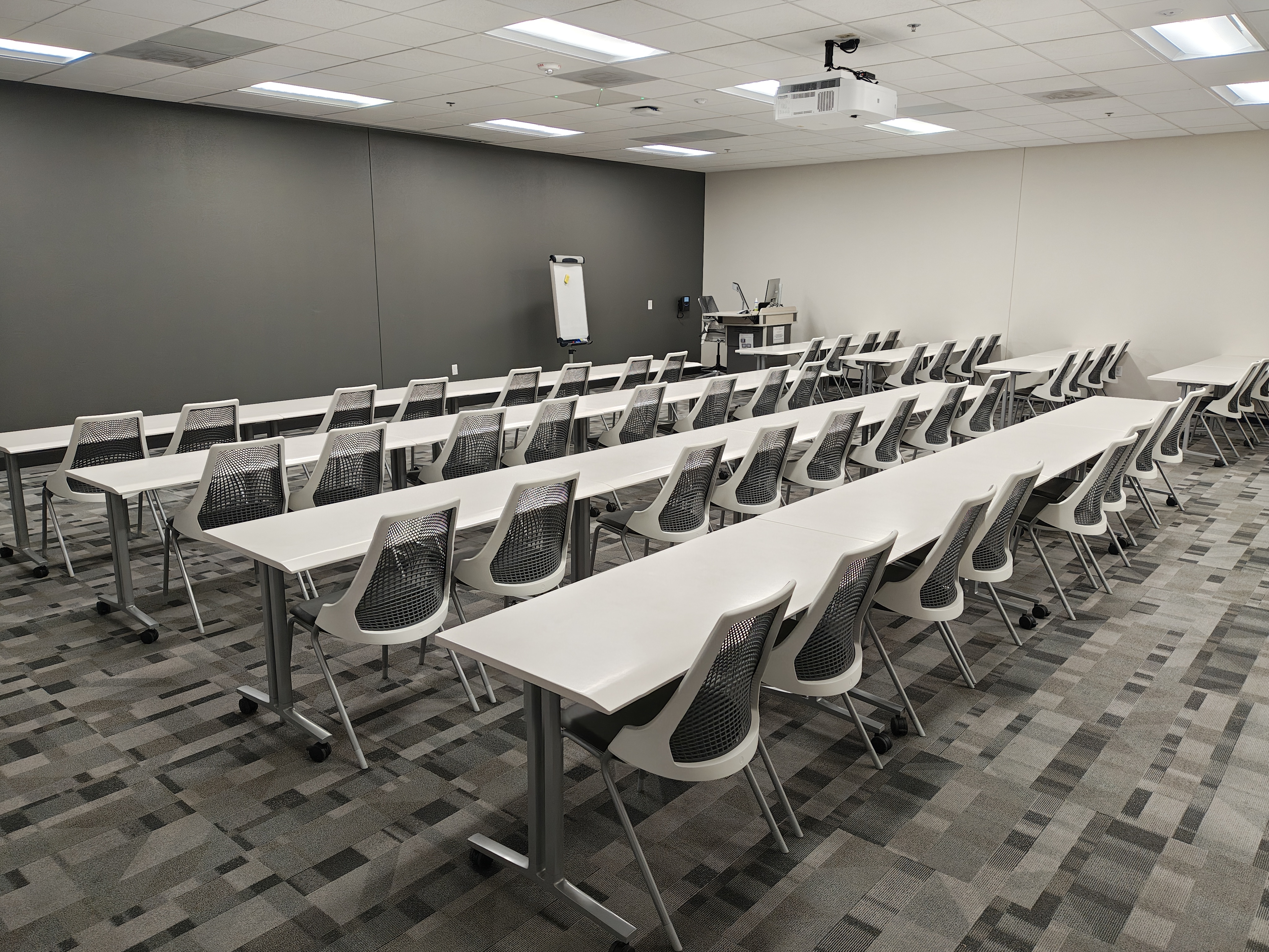 Empty classroom with rows of tables and chairs, and a lectern 